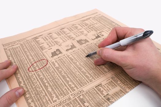 Male hands circle stock information in a newspaper against a white background.