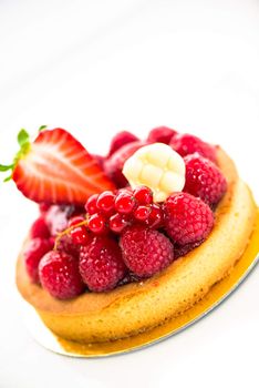 A small fruits tart with strawberry raspberry currant and a piece of chocolate on white background