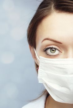 Female doctor on a blue blurred background in the face mask against flue infection