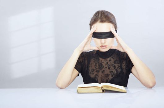 Woman with blindfold trying to read and understand foreign book.