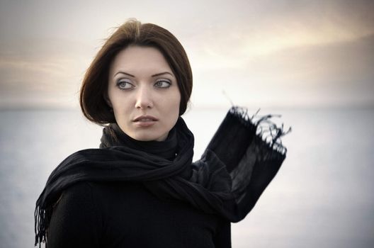 Romantic woman in black clothes with blown scarf outdoors at the sea