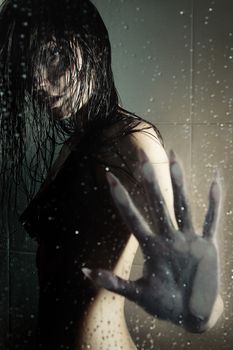 Female witch standing in the shower room behind the wet glass. Artistic darkness and texture added