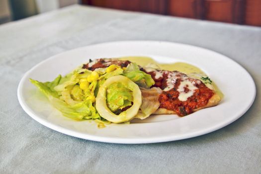 Horizontal white crockery on a table top with runner plated up white french crepe, tossed dressed salad, tomato herb vegetarian sauce white melted cheese and cheesy sauce.