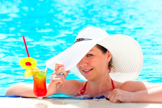 happy girl with a cocktail at the pool holding a hat hand