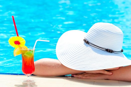 Girl with a cocktail in the pool covered her head a hat from the sun