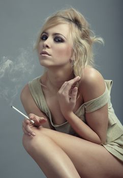 Blond lady sitting indoors and holding smoking cigarette. Natural light and colors
