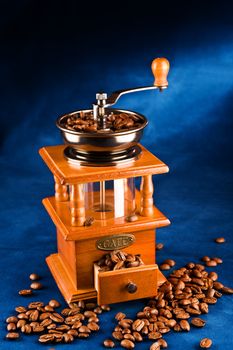 Manual coffee grinder with grains of coffee on a dark blue background