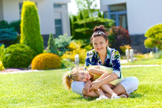 Happy girl with her mother sitting on the lawn in front new cottage