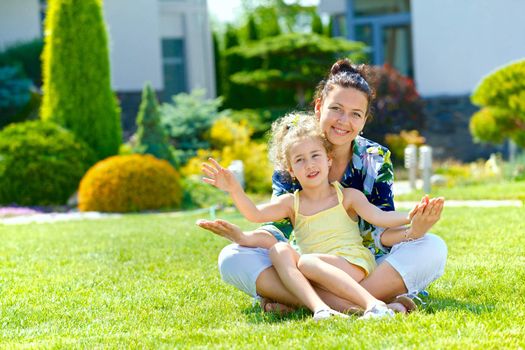 Happy girl with her mother sitting on the lawn in front new cottage