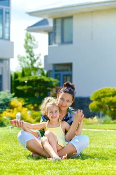 Happy girl with her mother sitting on the lawn in front new cottage. Vertical view