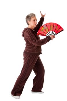 Beautiful Senior woman doing Tai Chi exercise with red dragon fan to keep her joints flexible, isolated.