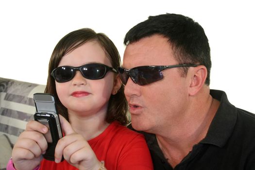 Cool dad and daughter with sunglasses on checking out her cell phone.
