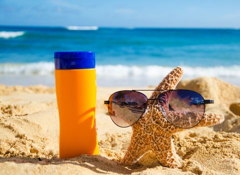 Sunscreen and starfish with sunglasses on sandy beach in Hawaii, Kauai