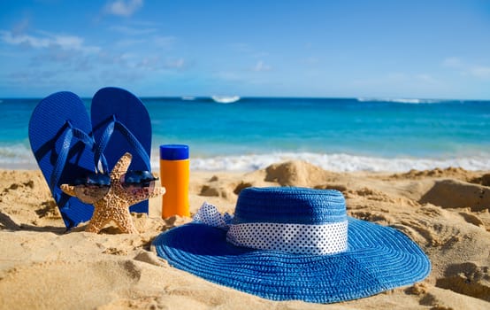 Blue Flip flops, sunscreen, woman's summer hat and starfish with sunglasses on sandy beach in Hawaii, Kauai