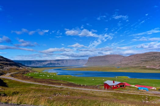 Beautiful red house in Iceland. Mountains, fjord, hay bales on the meadow in background.