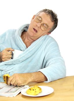 Nerdy middle aged man falls asleep at the breakfast table with a cup of tea and muffins.