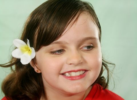 Little girl with a frangipani flower looking away to her left.