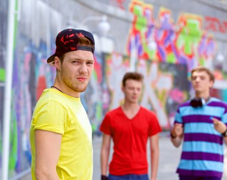 Happy teens boy with his friends by painted wall looking at camera
