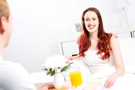 man brought his girlfriend breakfast in bed, holding a tray of juice and breakfast