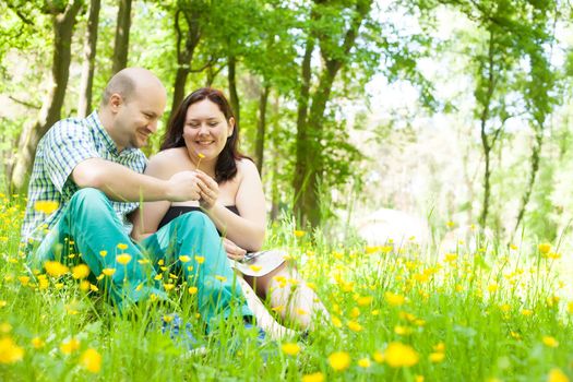 Happy young couple is sitting in a field of buttercups