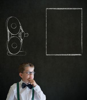 Thinking boy dressed up as business man with retro chalk film projector on blackboard background