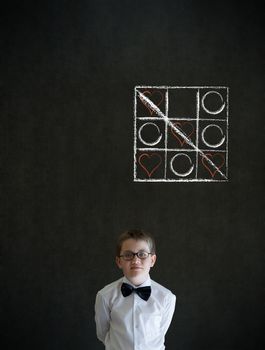 Thinking boy dressed up as business man with chalk tic tac toe love valentine concept on blackboard background