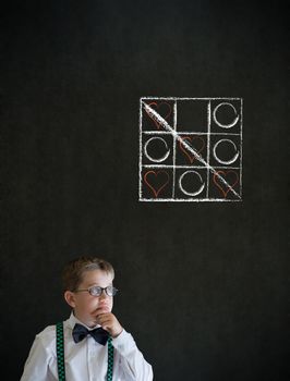 Thinking boy dressed up as business man with chalk tic tac toe love valentine concept on blackboard background