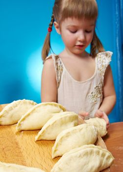 Smiling little girl kneading dough at kitchen with baking a pie