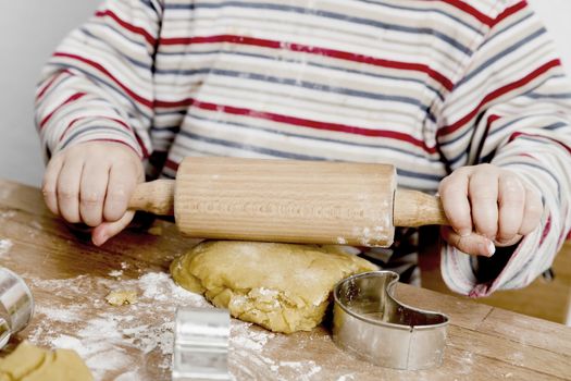 image of hands and desk. child is making cookies with a rolling pin