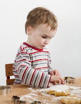 vertical image of 2 year old child making biscuit  at wooden desk