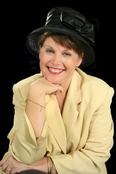 Smiling middle aged woman in a black hat with hand on chin.