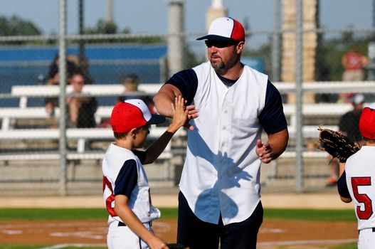 Baseball boy giving coach a high five during a game.