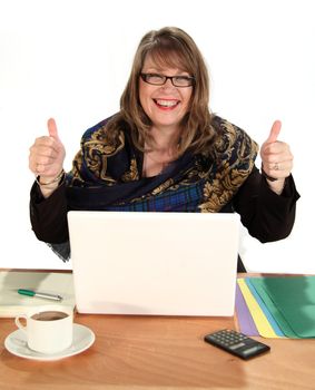 Middle aged business woman gives the thumbs up sitting at her desk in front of her laptop.