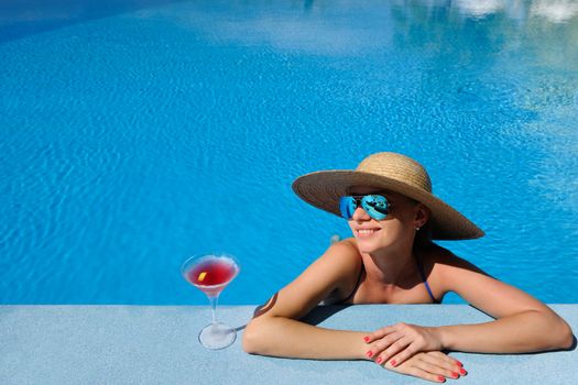 Woman in hat relaxing at the pool with cosmopolitan cocktail