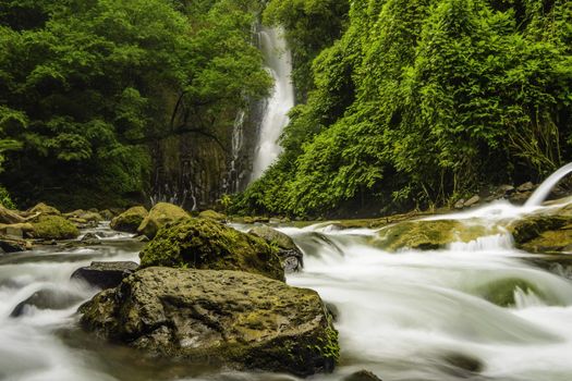 Fast flowing mountain stream in Costa Rica with a waterfall in the background.