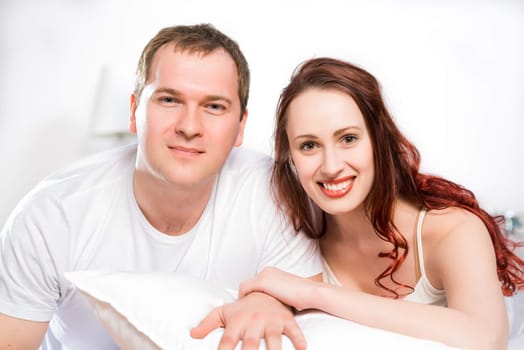 Young man and woman lying together in bed, smiling and happy