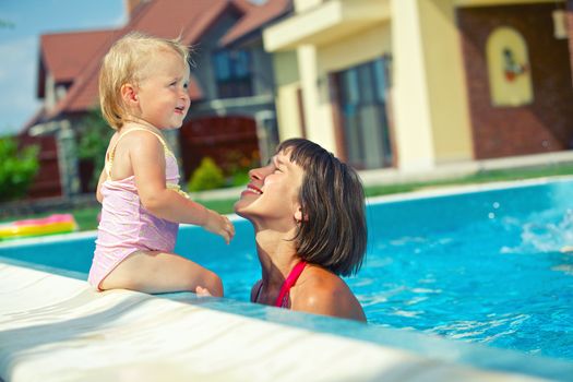 Summer vacation. Pretty little girl with her mother in swimming pool outdoors.