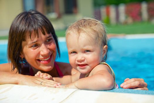 Summer vacation. Pretty baby girl with her mother in swimming pool outdoors