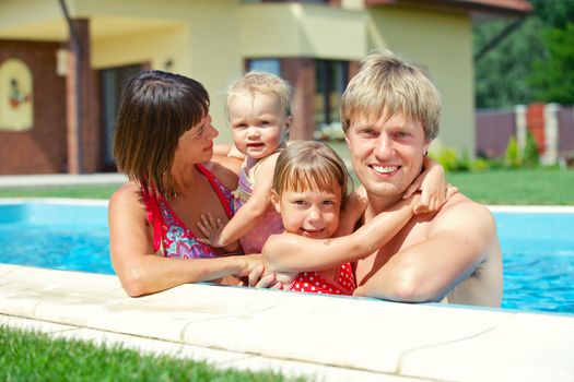 Summer vacation. Happy family of four in swimming pool outdoors
