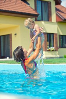 Summer vacation. Young woman plaing with her little daughter in swimming pool outdoors