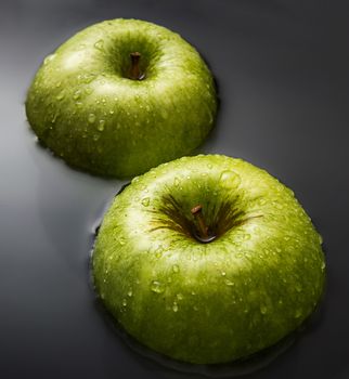 Two apples one over another inside water with drops