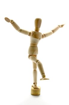Wooden manikin standing on one leg on coins