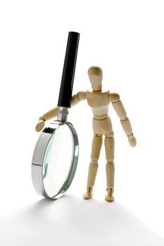 Wooden manikin and a magnification glass on white background