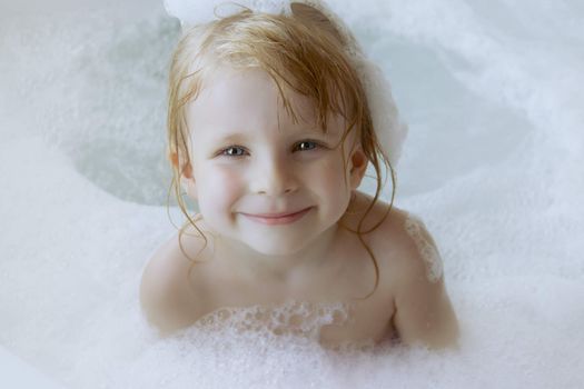 Smiling girl with a cap of foam on the head in bath