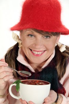 Middle aged woman rugged up for winter eating a hot cup of soup with a spoon.