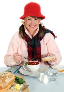 Middle aged woman rugged up for winter eating bread with a hot cup of soup.