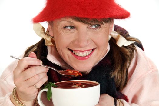 Middle aged woman rugged up for winter eating a hot cup of soup with a spoon.