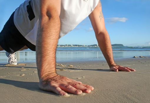 Man working out doing pushups on the beach in the early morning sun.
