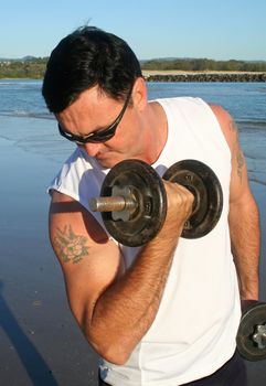 Man works out with weights on the beach just after sunrise.