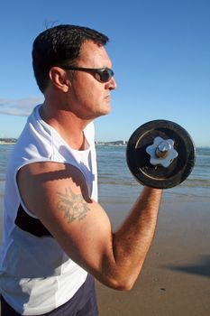 Man works out with weights on the beach just after sunrise.